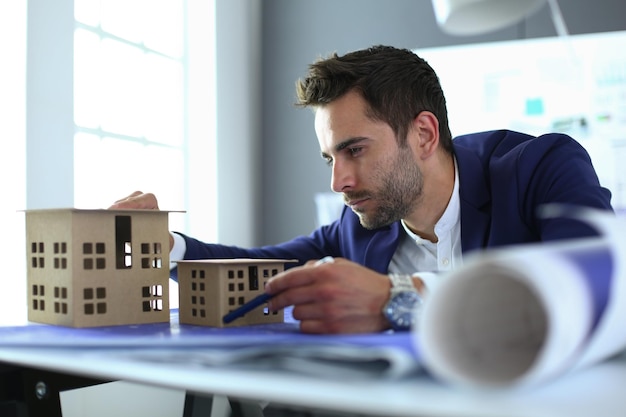 Businessman holding house miniature on hand standing in office