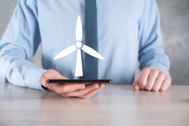 Businessman holding an icon of a windmill that produces environmental energy.