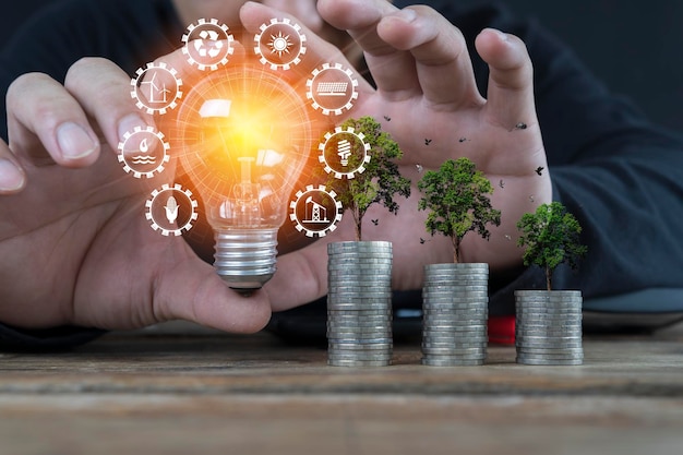 Businessman holding a light bulb and stacks of money growing with green trees Concept of pass and increase of renewable energy