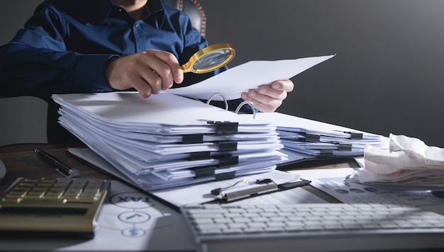 Businessman holding magnifying glass with documents.