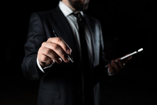 Businessman Holding Phone In One Hand With Other Pointing Important Message With Pen Executive In Suit Having Cellphone In One Palm And Crutial Announcement In Another