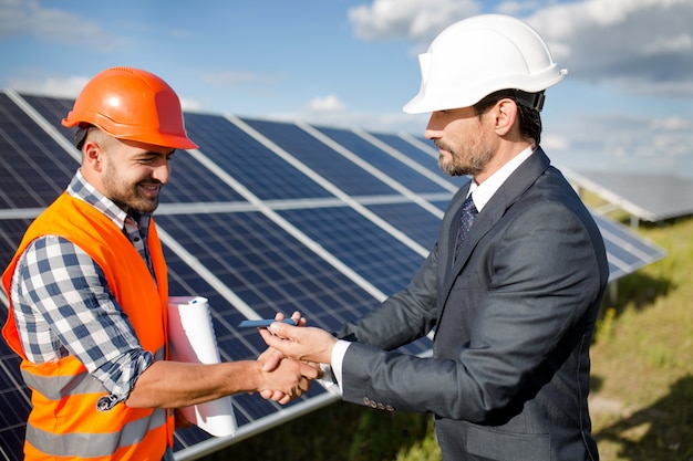 Businessman holding photovoltaic detail and shaking hand to a foreman.