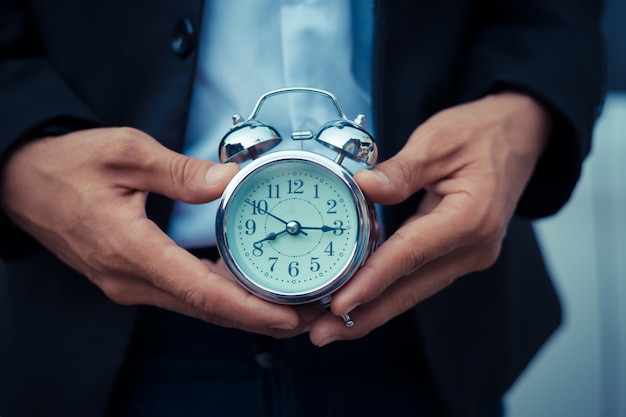 Businessman holding the retro clock in front of the white car