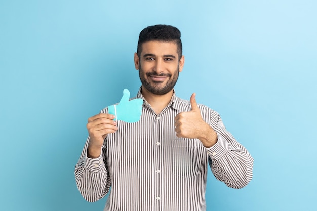 Businessman holding showing like or thumbs up paper shape sign looking at camera with toothy smile