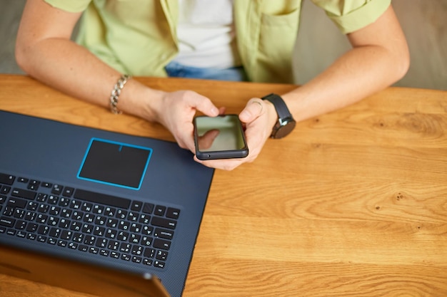 Businessman holding smartphone sitting in office using cell phone mobile apps and laptop