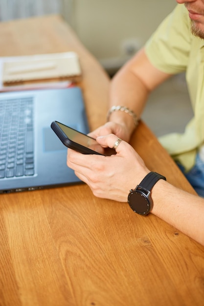 Businessman holding smartphone sitting in office using cell phone mobile apps and laptop