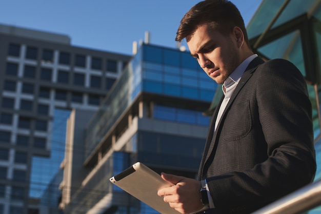 Businessman holding a tablet in hands on the background of buildings with glass facades