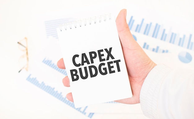 Businessman holding a white notepad with text CAPEX BUDGET business concept