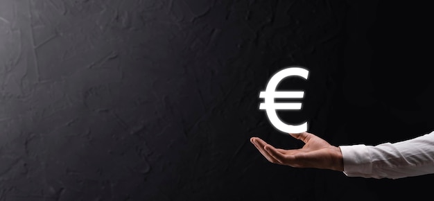 Businessman holds money coin icons EUR or Euro on dark tone background..Growing money concept for business investment and finance