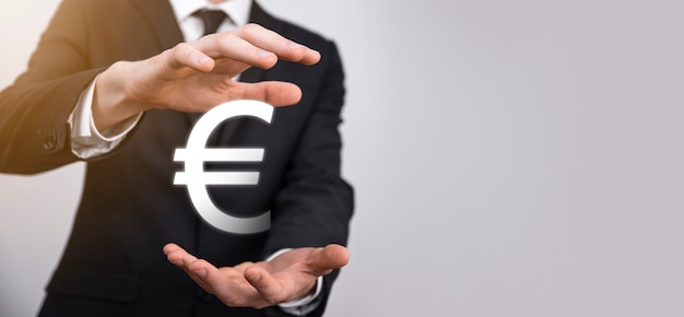 Businessman holds money coin icons EUR or Euro on dark tone background..Growing money concept for business investment and finance