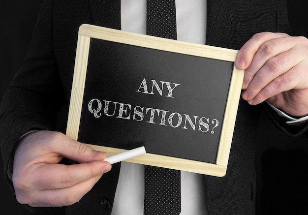 A businessman holds up a chalkboard with text Any Questions