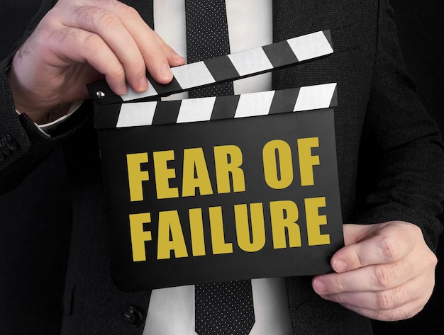 A businessman holds up a lapperboard with text Fear of failure