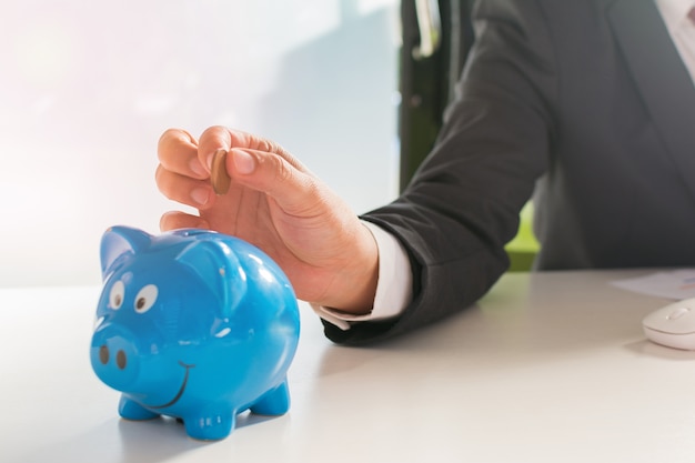 Businessman Inserting Coin In Piggybank and house Model