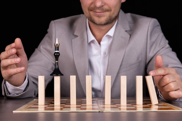 A businessman is building a pyramid of chess pieces and wooden blocks