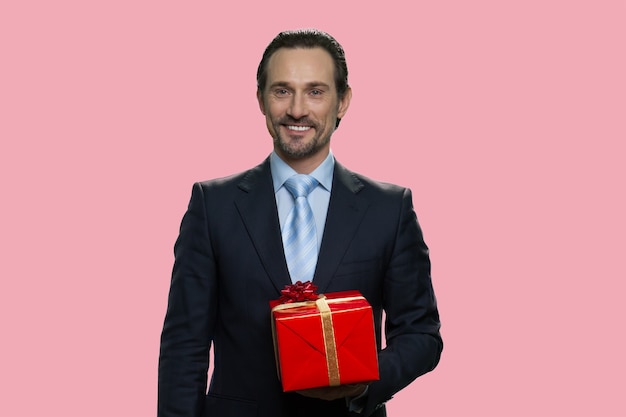 Businessman is holding a gift box. Isolated on pink background.