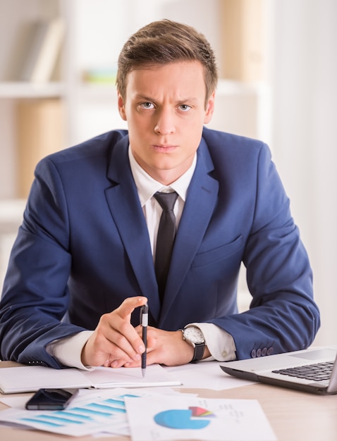 Businessman is looking at the camera sitting in his office.