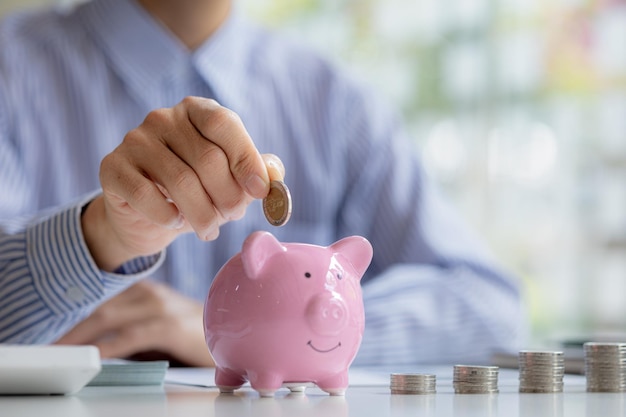 A businessman is putting coins into a pink pig piggy bank he is saving for investments money growth stock investments The idea of investing money to make it worthwhile to grow and be sustainable