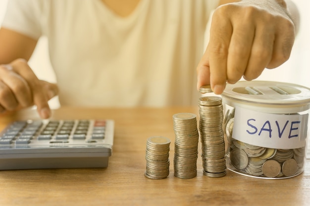 The businessman is putting coins into the stacked and  accummulate in column that represent money saving or financial planning idea for economy.