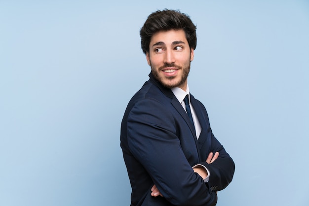 Businessman over isolated blue wall with arms crossed and happy