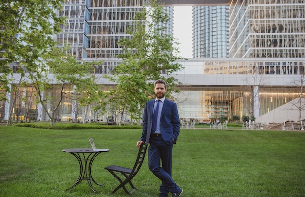 Businessman on large grass field near modern office building. Business man in park of megapolice.