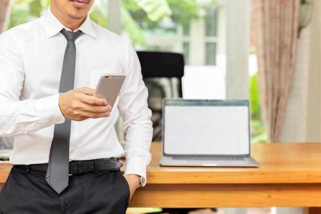 Businessman looking at cell phone with laptop on wooden table at office