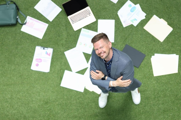 Businessman looks up on green lawn with laptop and financial business chart