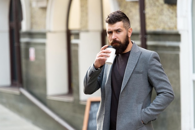 Businessman lumbersexual appearance enjoy coffee break out of business center Relax and recharge Man bearded hipster drinking coffee paper cup One more sip of coffee Drinking coffee on the go