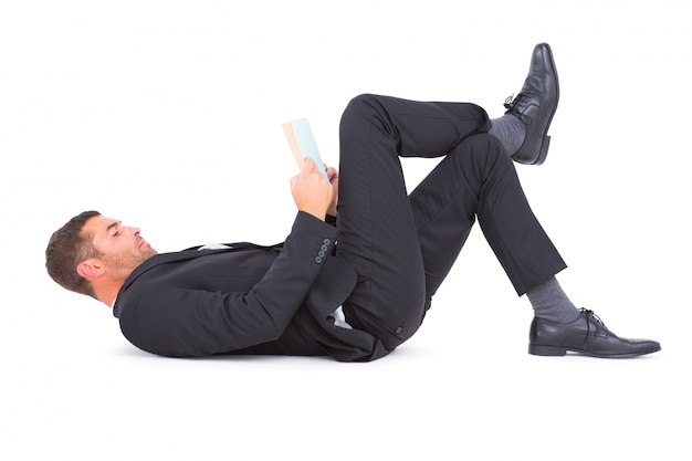 Businessman lying on the floor reading book 