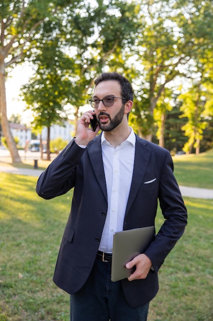 Businessman in the park answers his cell phone while walking to get away from the office