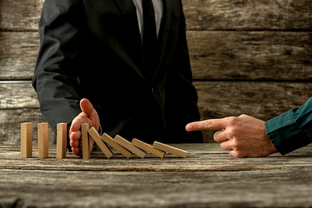 Photo businessman pointing to falling dominos and his partner stopping them in a conceptual image of cooperation and mentor