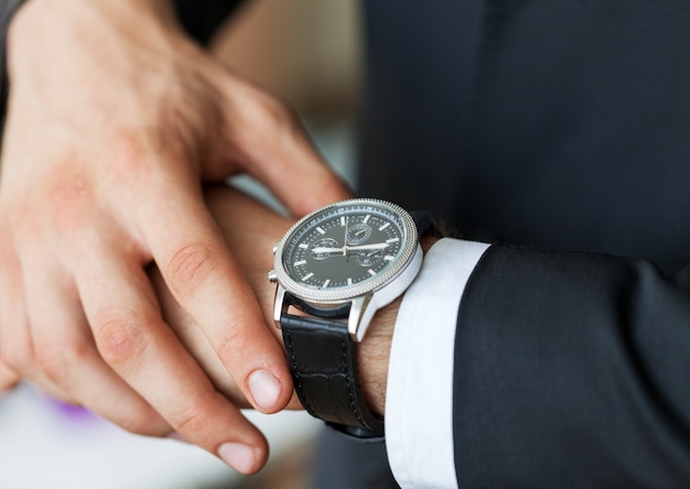 Businessman pointing at hand watch on grey wall background, close-up