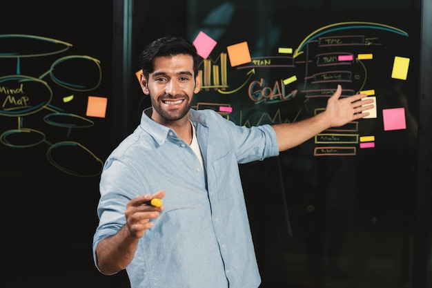 Businessman pointing at marketing statistic while looking at camera Tracery