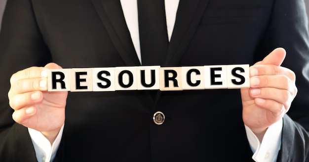 Photo businessman protecting his resources holding his hands above a row of wooden blocks with the word resources