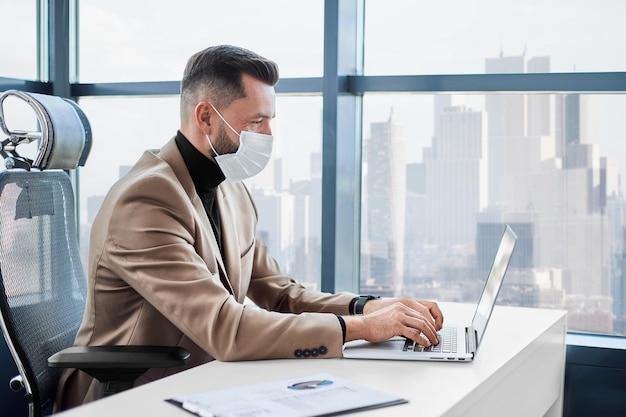 Businessman in a protective mask working on a laptop in the office