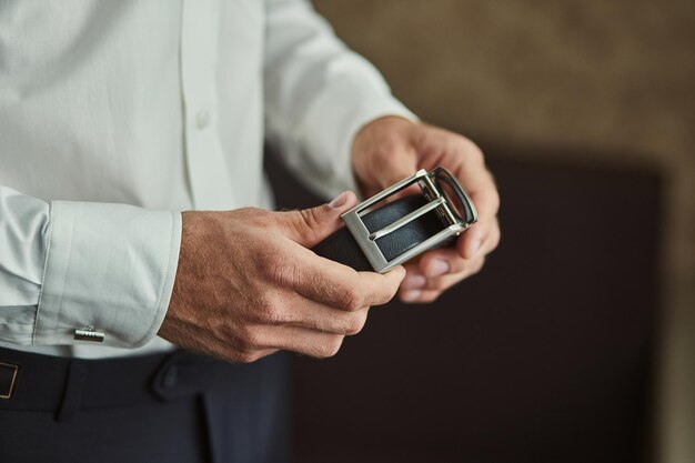 Businessman putting on a belt fashion and clothing conceptgroom getting ready in the morning before ceremony