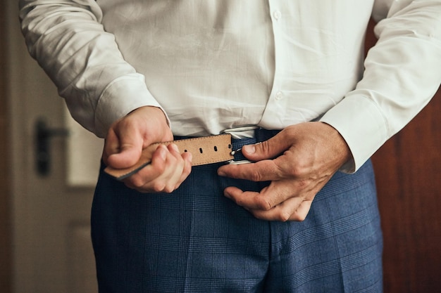 Businessman putting on a belt fashion and clothing conceptgroom getting ready in the morning before ceremony