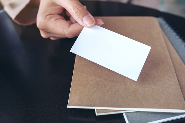 A businessman's hand holding and giving empty business card with notebooks on table