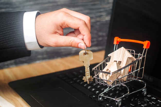 Photo the businessman's hand holds the keys near the wheelbarrow with the houses.