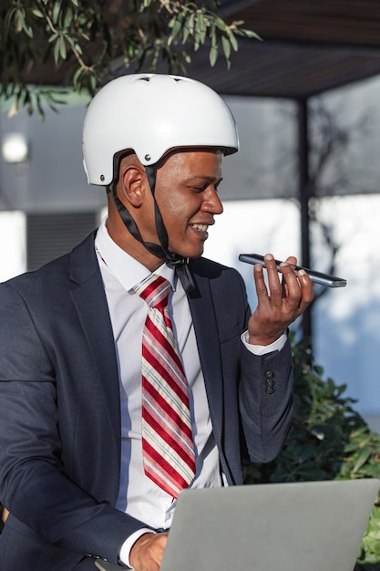 Businessman sending a voice message while working on a laptop sitting outdoors