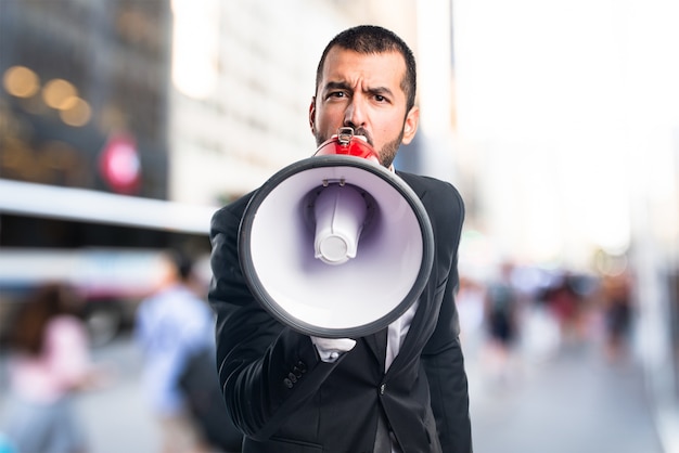 Businessman shouting by megaphone on unfocused background