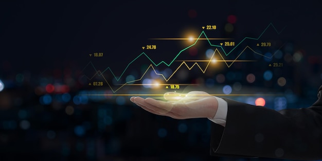 Businessman showing a growing virtual hologram stock chart on the hand with dark tone background trading finance and business image