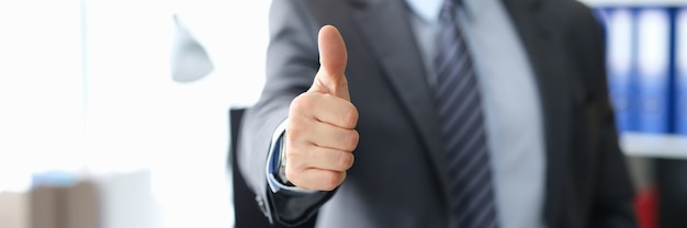 Businessman showing thumbs up gesture while standing in office