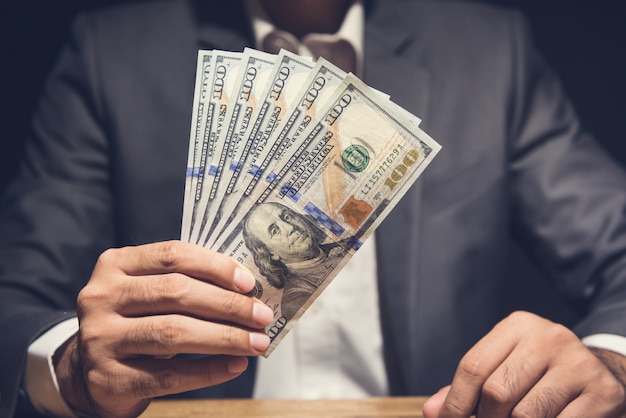 Businessman showing US dollar bills at the table in dark