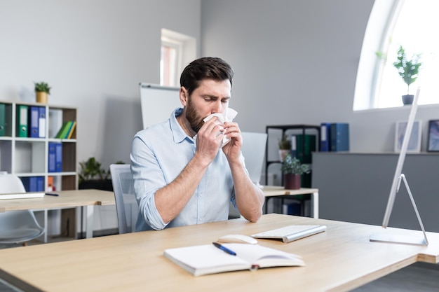 Businessman sick in the office man with allergies sneezes sitting at a table with a computer