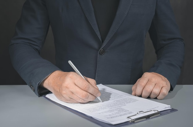 Businessman signs contract Holding pen in hand Businessman signing contract at table Signing legal document dark background