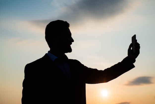 Businessman silhouette making selfie on phone on sky background. confidence and success. successful future. agile business. loneliness. need the inspiration. man feel motivation. modern technology.