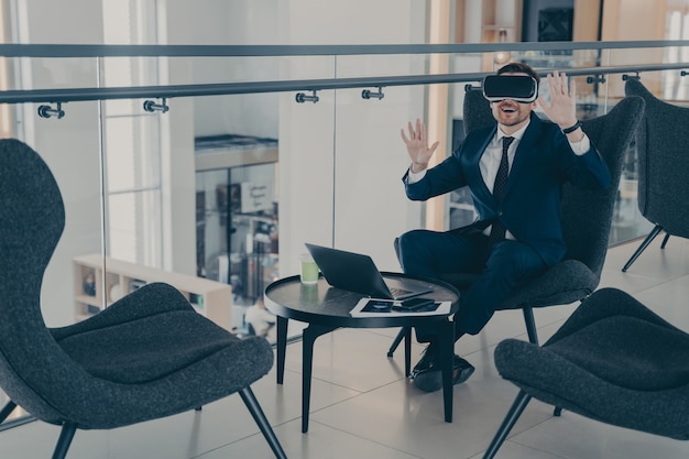 Businessman sitting in reception area of office centre during his coffee break in VR headset