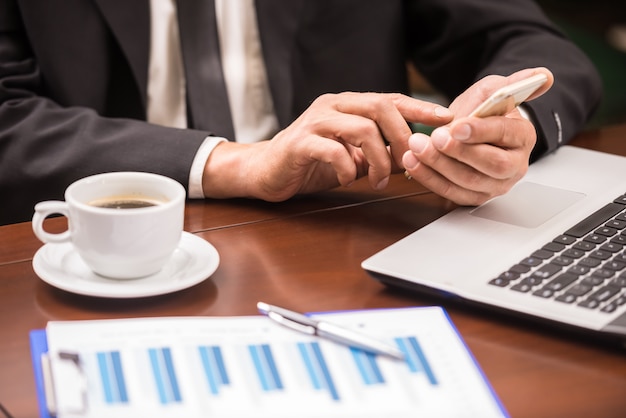 Businessman sitting at the table in cafe and using phone.