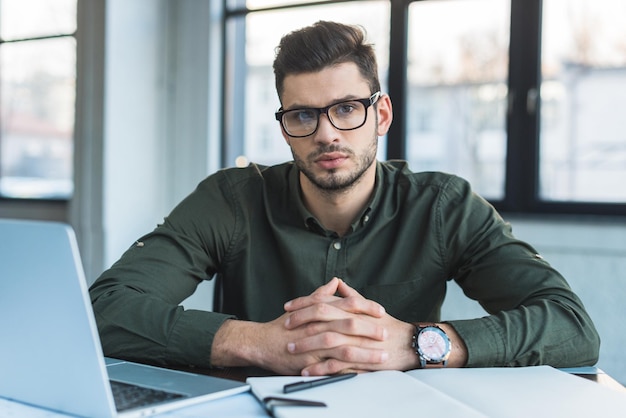 businessman sitting at table in office and looking at camera