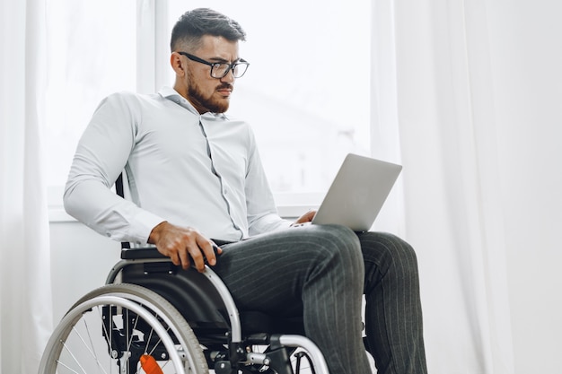 Businessman sitting in wheelchair and using laptop at home